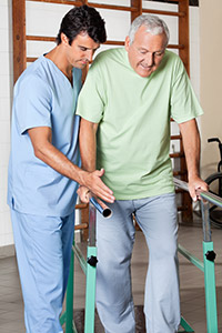 Picture of a male Nurse Therapist helping assist an older male on some rails he is holding on to as he walks.